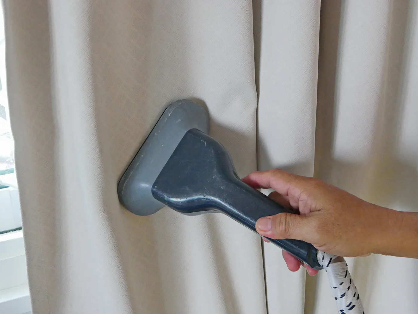 A hand-held steamer being used on a curtain